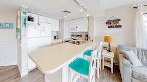 A modern kitchen with a central island, white cabinetry, and a dining area with a striped sofa and teal chairs.