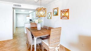 Een eetruimte met een houten tafel, rieten stoelen, een hanglamp en spiegels aan de muur.