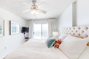 Ein Hotelzimmer mit Bett, Deckenventilator, Fernseher und einem Balkon mit Vorhängen.