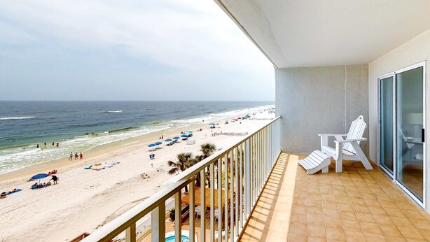 Een balkon met uitzicht op een strand, witte stoelen en een zwembad.
