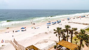Een strand met parasols, palmbomen en een houten constructie.