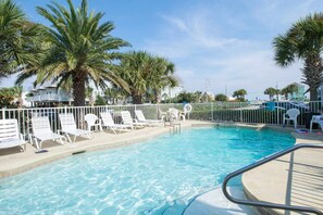 A swimming pool with white lounge chairs, palm trees, and a white fence. - Fun Seahorse condo with gas grill, W&D, & pool access - walk to West Beach (Gulf Shores)