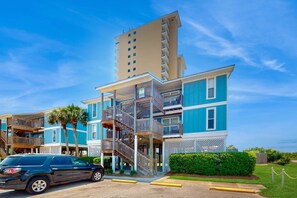 A multi-story hotel with a blue facade, a central staircase, and a parking lot. - Fun Seahorse condo with gas grill, W&D, & pool access - walk to West Beach (Gulf Shores)