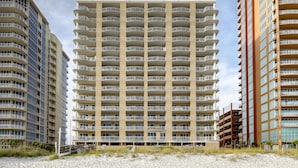 Un hotel de varios pisos con balcones, vistas a la playa y arena en primer plano.