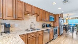 Una cocina con armarios de madera, encimeras de granito, lavavajillas, refrigerador y microondas.