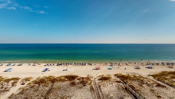 A beach with a wooden walkway leading to the shore, sandy beach, and umbrellas. - Delightful beachfront condo w/ a furnished balcony, views, & a shared pool (Gulf Shores)