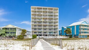 A beachfront hotel with multiple balconies, a wooden boardwalk, and a clear blue sky. - Delightful beachfront condo w/ a furnished balcony, views, & a shared pool (Gulf Shores)
