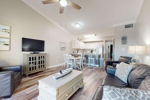 Una sala de estar con televisor, un comedor y una cocina al fondo.