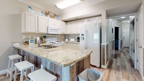 A kitchen with white cabinets, a granite countertop, and a wooden island with stools. - Delightful beachfront condo w/ a furnished balcony, views, & a shared pool (Gulf Shores)