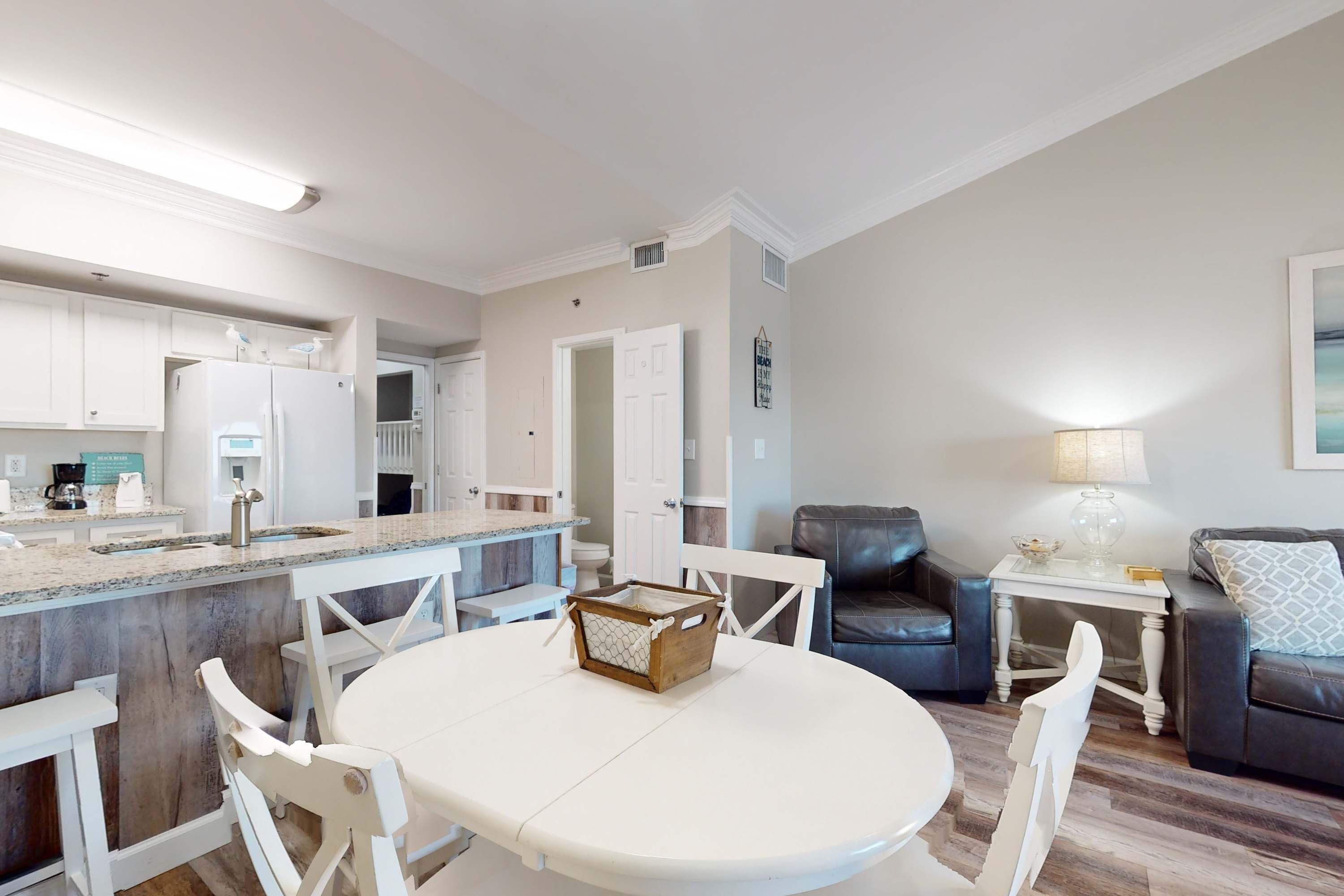 A modern kitchen with white cabinetry, a central island, and a dining area with a round table and chairs.