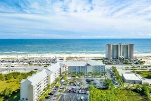 A hotel with a parking lot, a beach, and a view of the ocean. - Snowbird-Friendly Condo w/Beach Access, Shared Outdoor Pool, Private Balcony (Orange Beach)