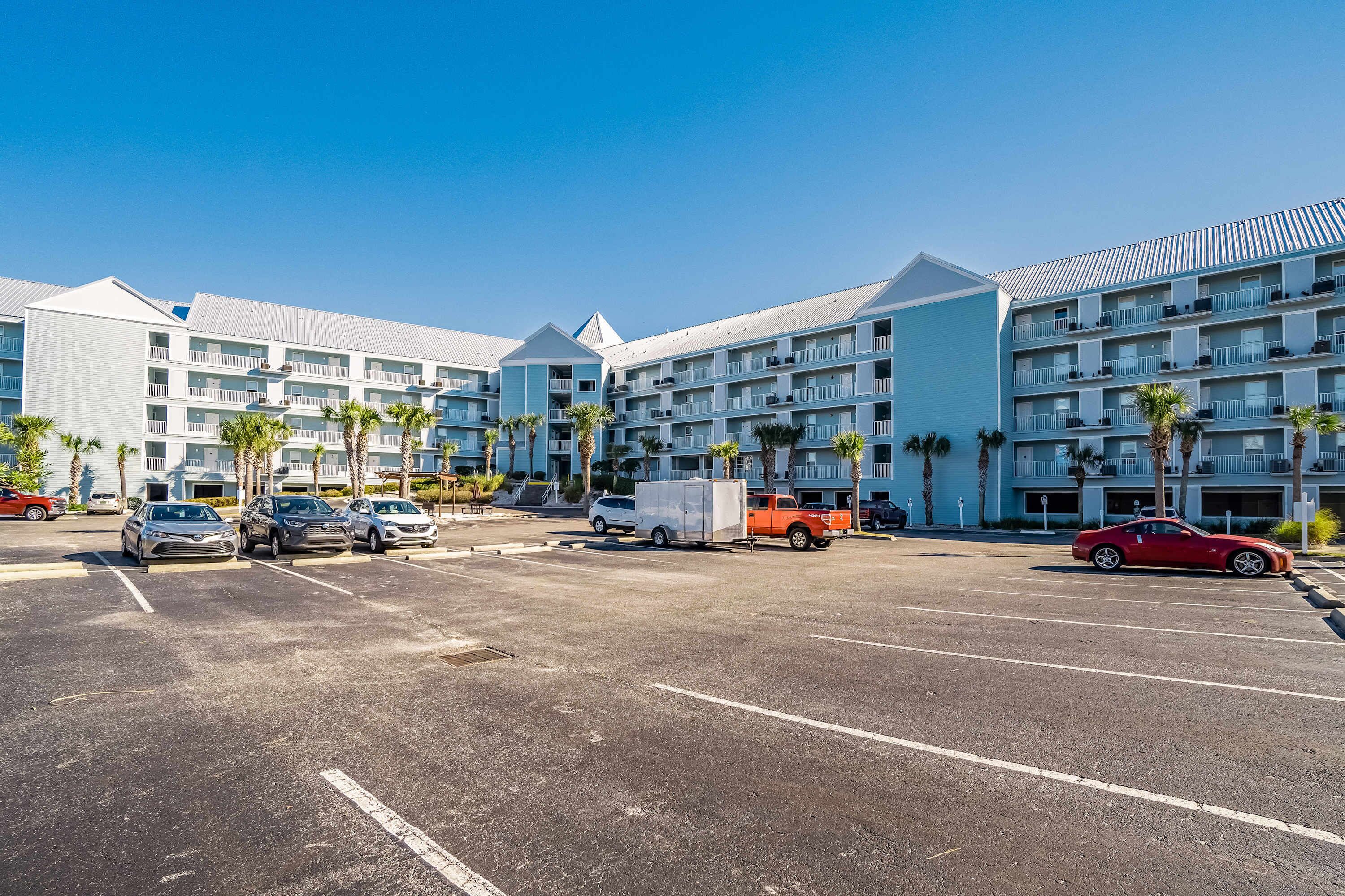 Ein Hotel mit mehreren Stockwerken, einem Parkplatz mit Autos und Palmen.