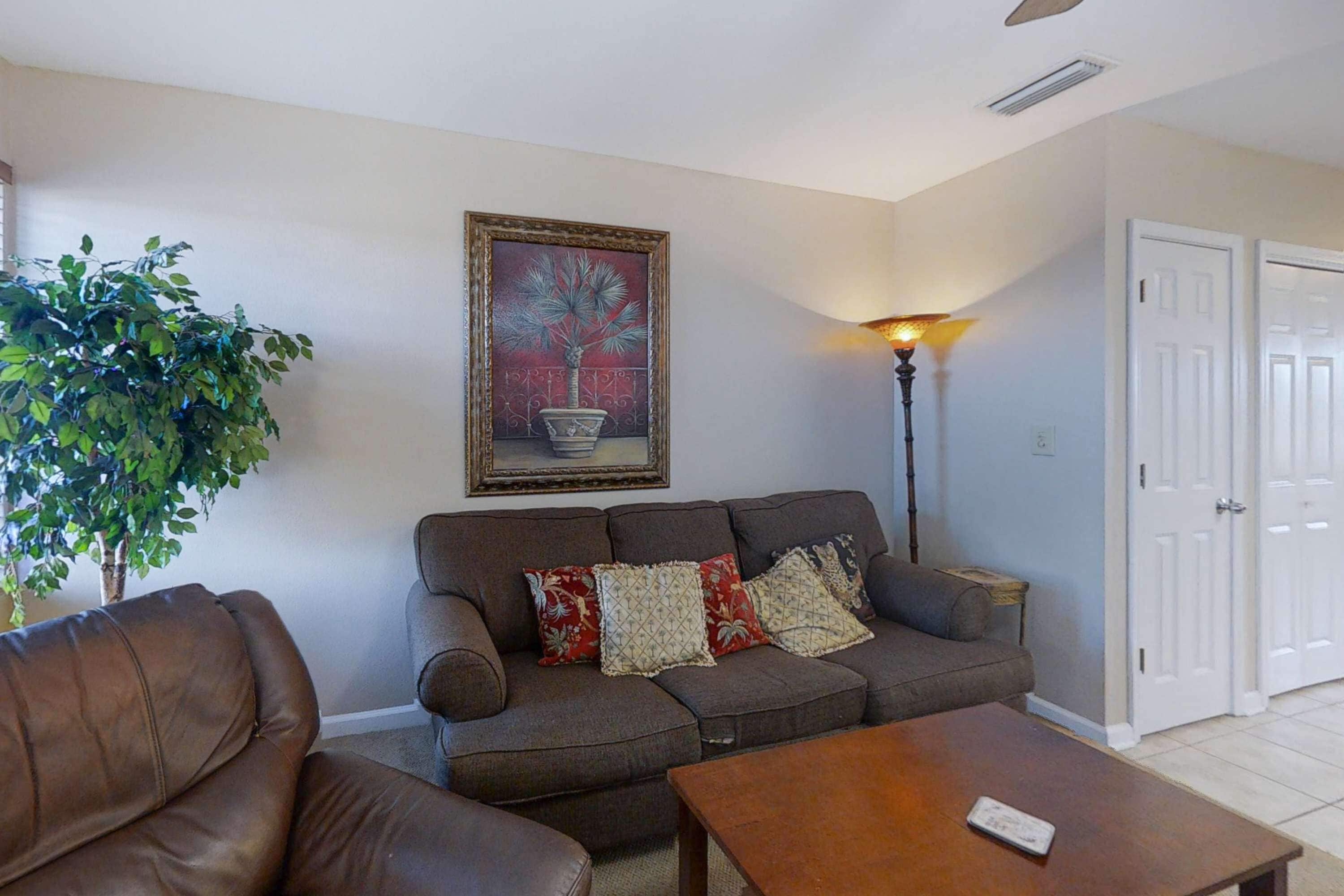 A living room with a brown leather sofa, a wooden coffee table, a floor lamp, and a painting on the wall.