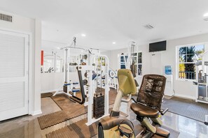 A gym with exercise equipment, a television, and a view of palm trees. - Snowbird-Friendly Condo w/Beach Access, Shared Outdoor Pool, Private Balcony (Orange Beach)