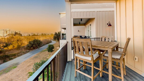 Eine Holzterrasse mit Tisch und Stühlen, mit Blick auf einen Strand und Gebäude.
