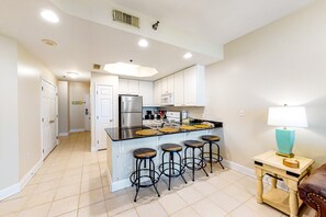 A modern kitchen with a central island, bar stools, a refrigerator, and a microwave. - Ocean & Gulf front condo w furnished balcony, shared in & outdoor pools, & hot tub (Gulf Shores)