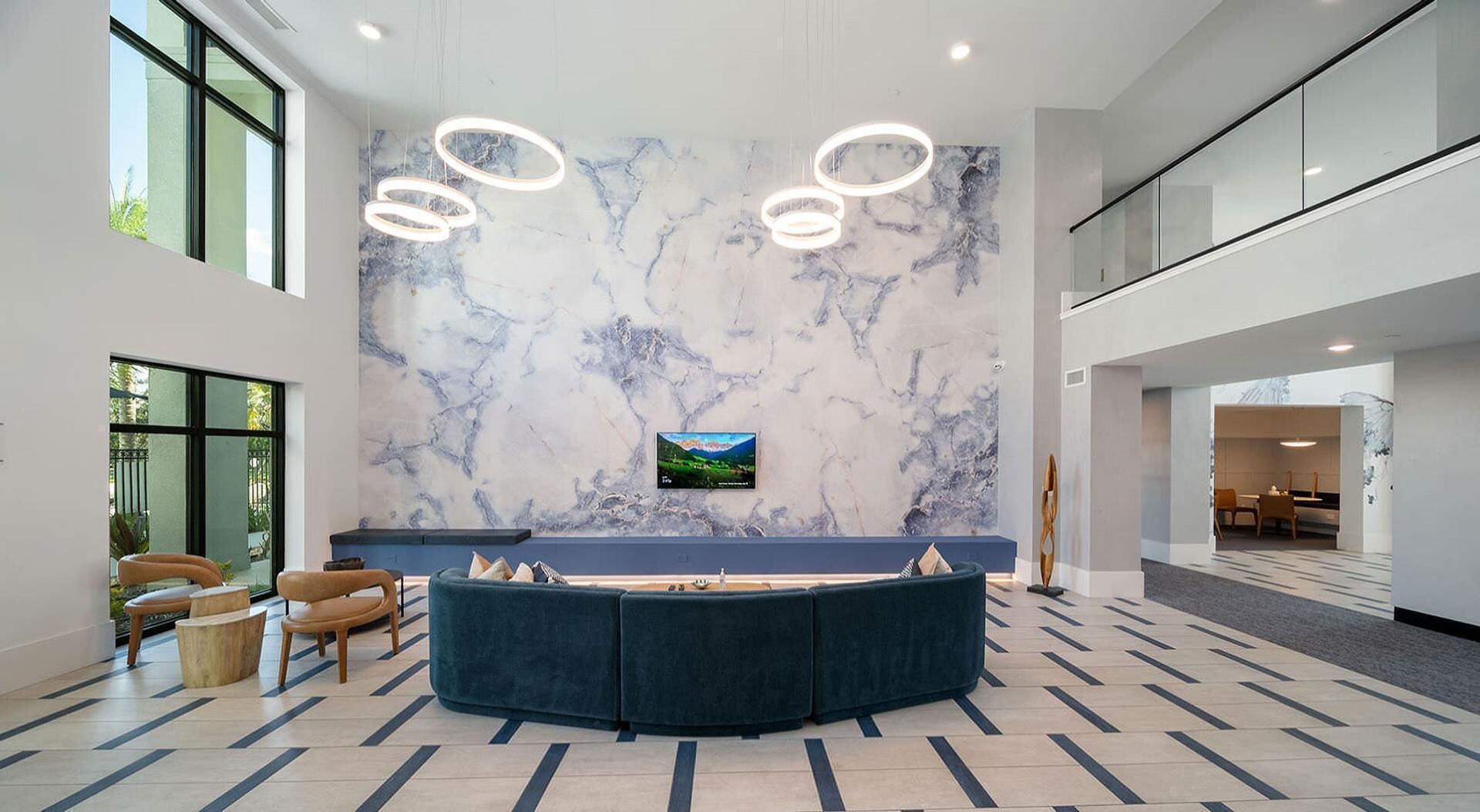 A modern lobby with a marble wall, a large seating area, and a television screen.