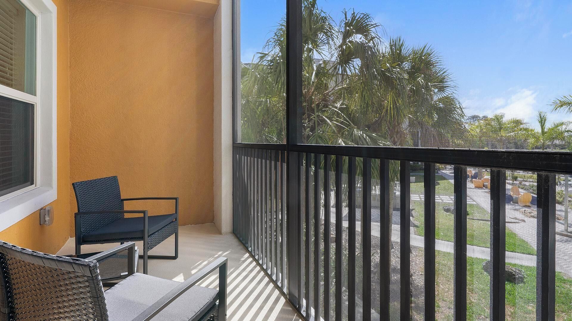 Ein Balkon mit Stuhl, Fenster und Blick auf Palmen und eine Straße.