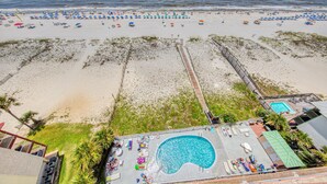 Un complejo turístico en la playa con piscina, sombrillas y un paseo marítimo.