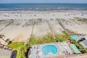 A beach resort with a swimming pool, beach umbrellas, and a boardwalk. - Beachfront, corner condo w a furnished balcony, shared pool, & grilling area (Gulf Shores)