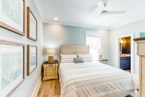 A bedroom with a bed, bedside tables, a ceiling fan, and framed artwork on the wall. - Luxurious, two-story cottage near the beach w a full kitchen & shared pool (Gulf Shores)