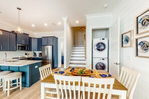 A modern kitchen with dark cabinets, a central island, and a dining area with a table set for two. - Luxurious, two-story cottage near the beach w a full kitchen & shared pool (Gulf Shores)