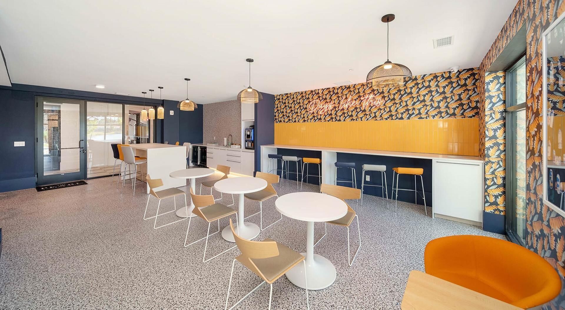 A modern dining area with round tables and chairs, a kitchen area, and a patterned wall.
