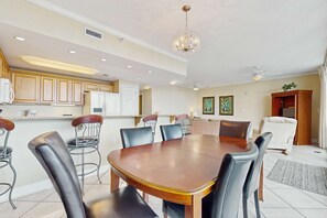 A dining area with a wooden table and chairs, a kitchen with wooden cabinets, and a ceiling fan. - Gulf condo w/ private balcony, stunning views, pools, & sauna (Gulf Shores)