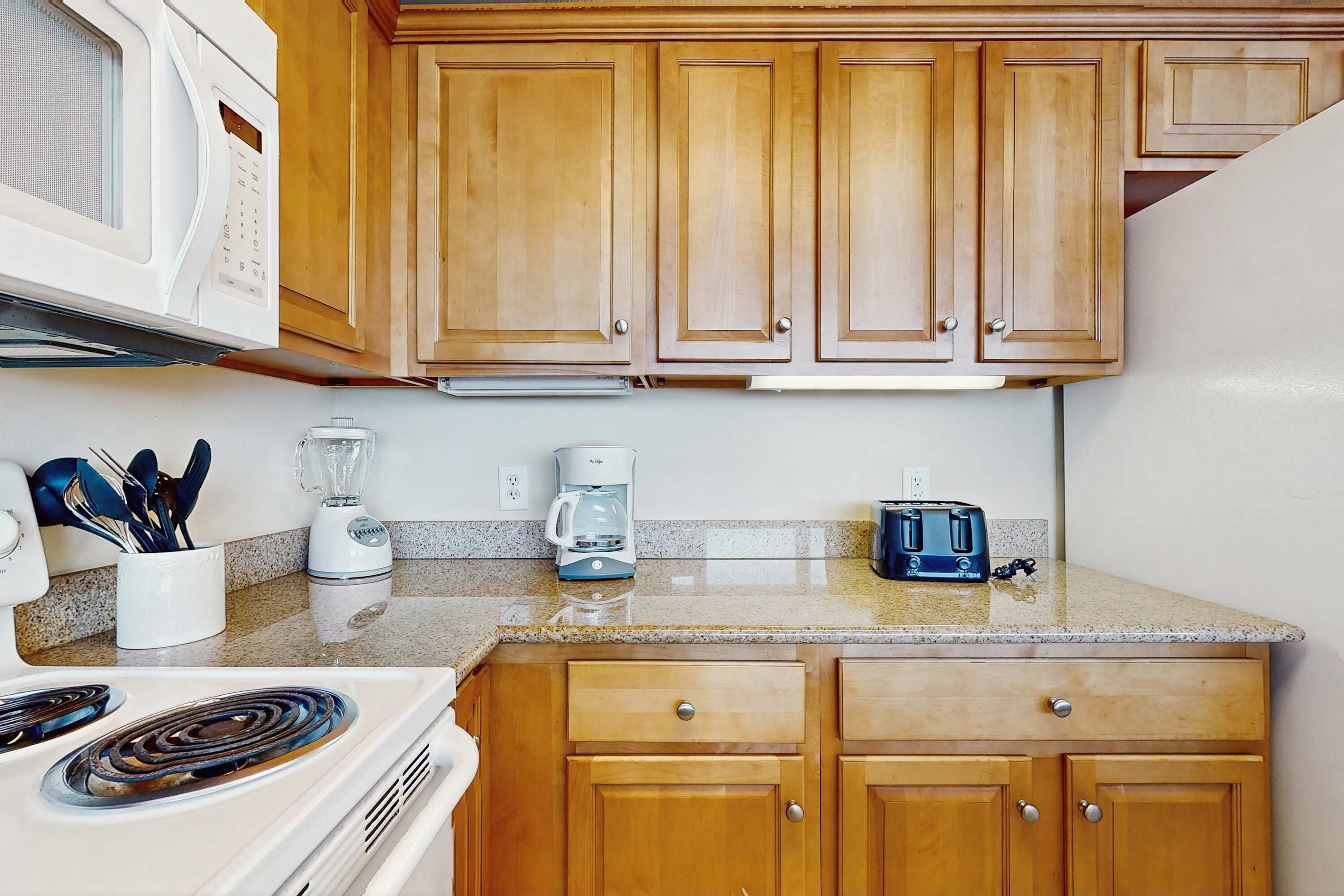 Una cocina con armarios de madera, microondas, cafetera, tostadora y estufa.