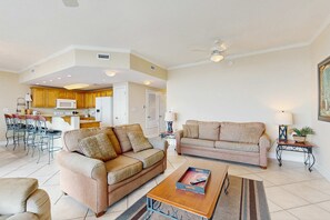 A living room with two sofas, a coffee table, and a dining area with chairs and a kitchen in the background. - Gulf condo w/ private balcony, stunning views, pools, & sauna (Gulf Shores)