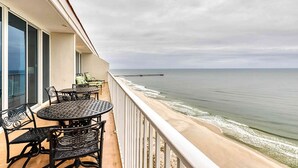 Ein Balkon mit Tisch und Stühlen mit Blick auf einen Strand und einen Steg.