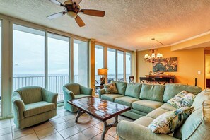 A spacious living room with a view of the ocean, a ceiling fan, and a chandelier. - Beachfront penthouse w/ amazing view, multiple pools, hot tubs, gym & sauna (Gulf Shores)