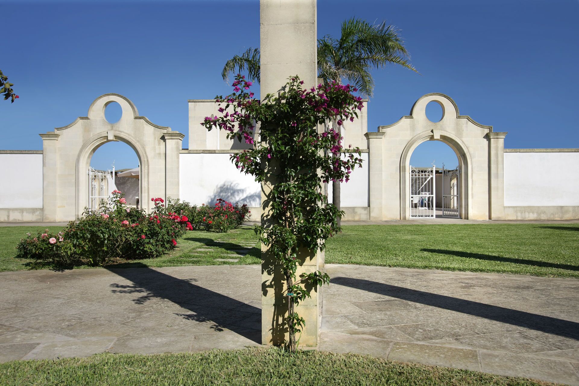 A courtyard with a central column, surrounded by a low wall and a large archway structure.