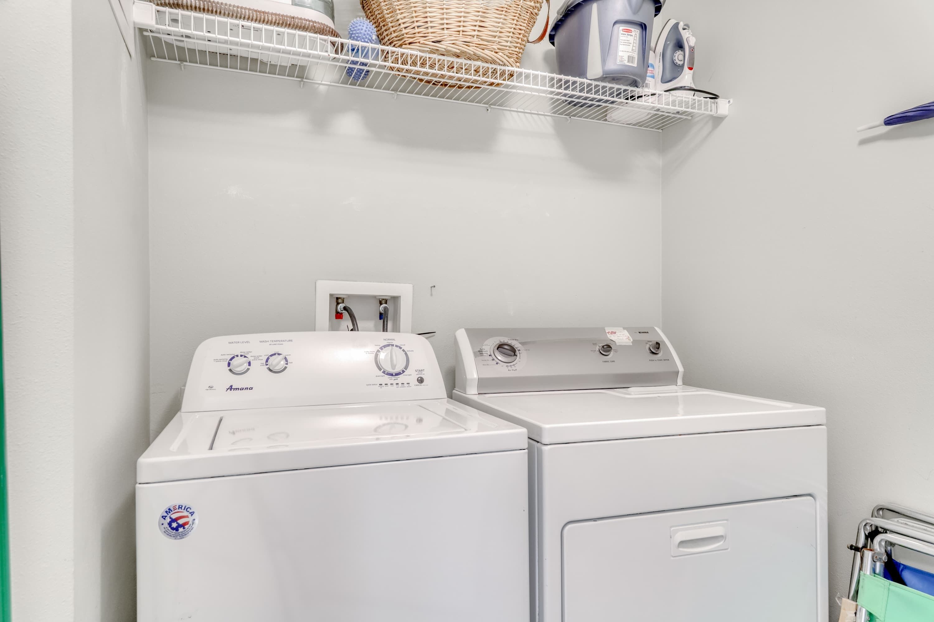 A laundry area with two white front-loading washers and dryers, a white shelf with laundry supplies, and a basket.