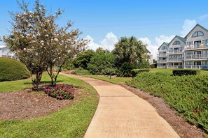 A landscaped pathway leading to a building with multiple balconies and a well-maintained garden.