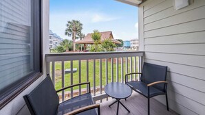 A balcony with two chairs and a small table, overlooking a grassy area and buildings. - Cozy waterfront getaway with pools, hot tub & tennis courts (Fort Morgan)
