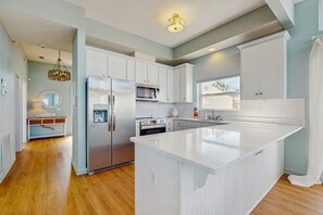 A modern kitchen with white cabinetry, a large island, stainless steel appliances, and a hanging light fixture. - Beautiful Water Front Home in Historic Fairhope (Fairhope)