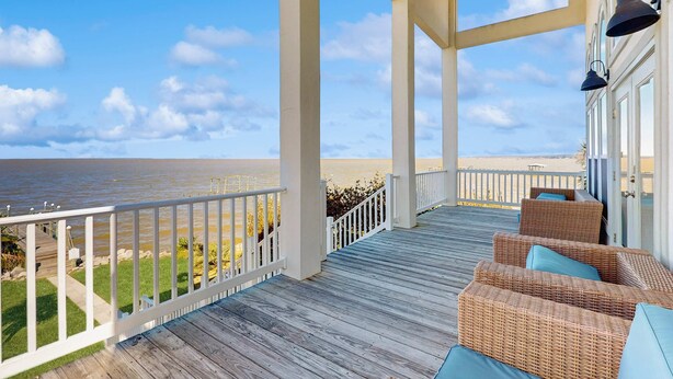 Eine überdachte Terrasse mit Korbmöbeln und Blick auf das Meer.
