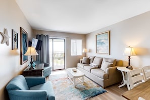 A living room with a sofa, armchair, coffee table, and lamps. There is a balcony with a view. - Snowbird-friendly hotel suite with beach access, shared pool and dining (Fort Morgan)