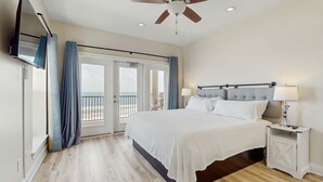 Un dormitorio con cama, ventilador de techo, televisor y balcón con cortinas.