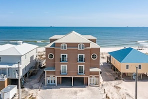 A multi-story beachfront building with a central entrance, balconies, and a beachside location. - Luxury Beachfront Estate in Fort Morgan | Private Pools, Elevators and Wedding-Friendly (Fort Morgan)