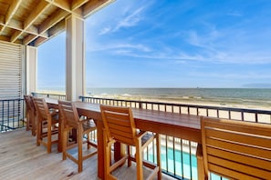 A wooden deck with a table and chairs overlooking a beach. - Luxury Beachfront Estate in Fort Morgan | Private Pools, Elevators and Wedding-Friendly (Fort Morgan)