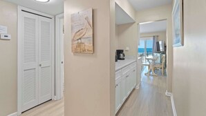 Un couloir avec une porte blanche, un tableau et un coin cuisine comprenant une table et des chaises.