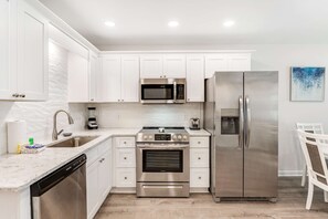 A modern kitchen with white cabinets, stainless steel appliances, a dishwasher, and a coffee maker. - Beach-view retreat with shared gym, pool, and beach access (Fort Morgan)