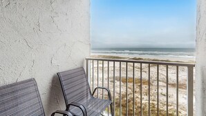 A balcony with two chairs, a white textured wall, and a view of the beach. - Waterfront retreat with Gulf views, pools (Fort Morgan)