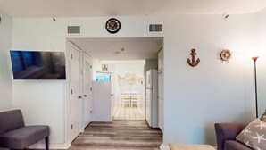 A living room with a flat-screen TV, a sofa, a wooden coffee table, and a hallway leading to a kitchen. - Waterfront retreat with Gulf views, pools (Fort Morgan)
