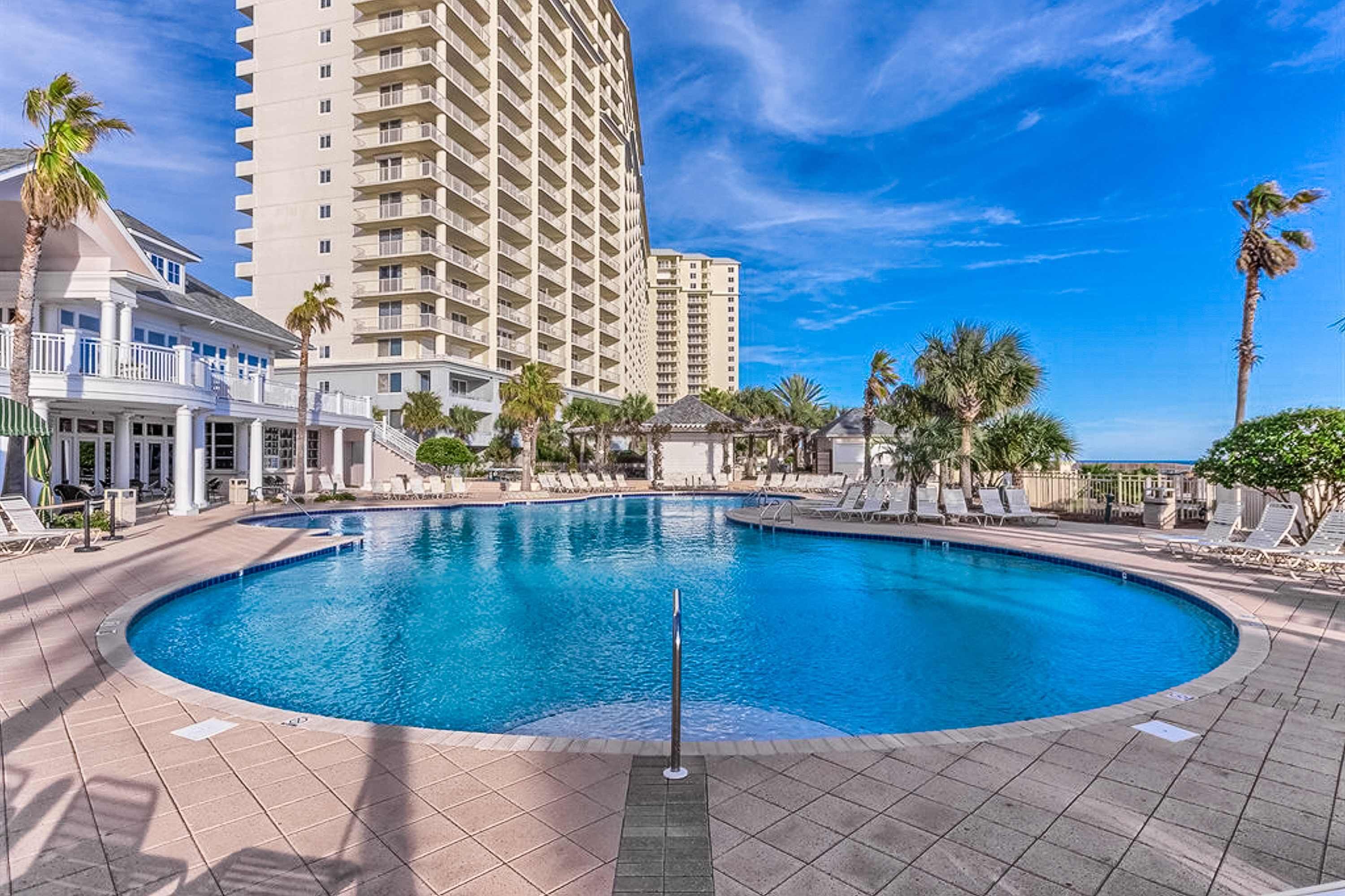 A pool area with a circular pool, lounge chairs, palm trees, and tall buildings in the background.