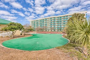 Un terrain de golf avec un gazon verdoyant, un bâtiment doté de nombreux balcons et un palmier.