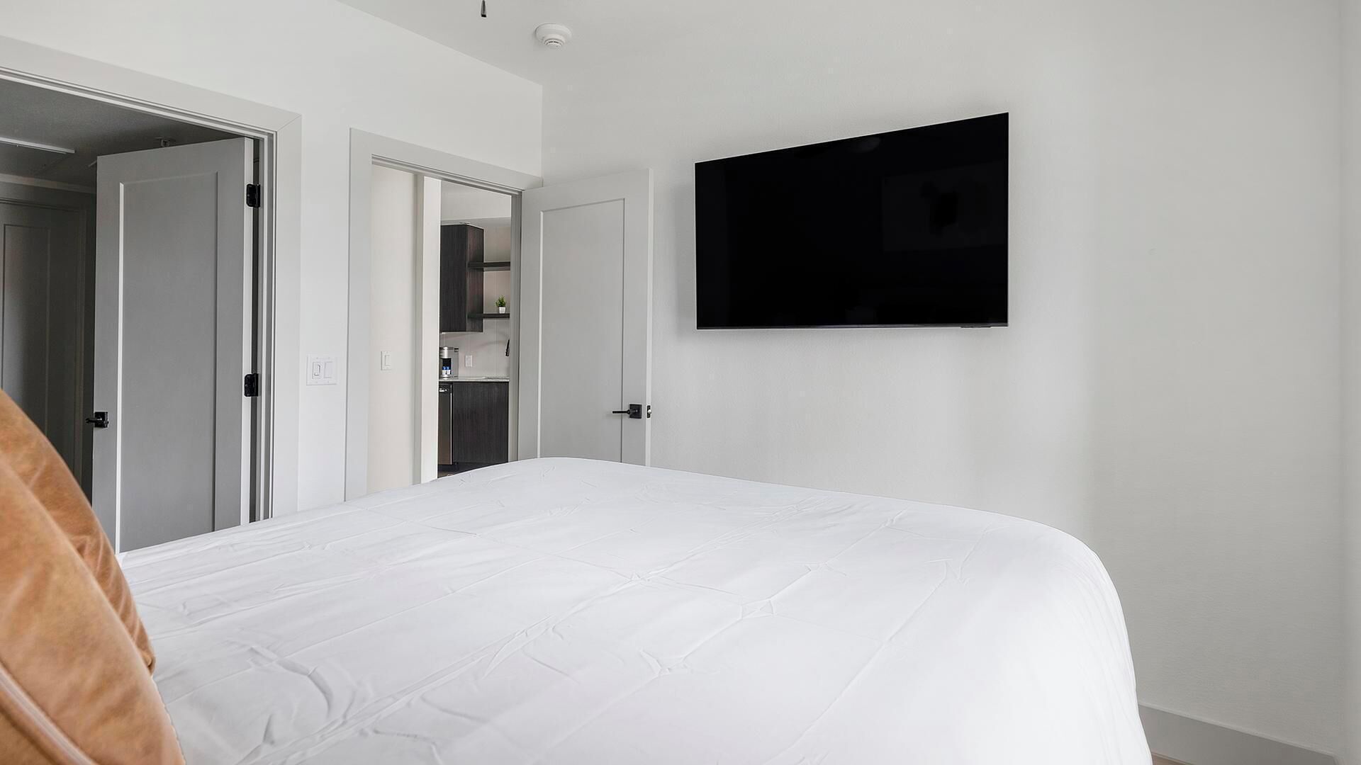 Una camera da letto con un letto, una TV fissata al muro e una porta che dà su un bagno.