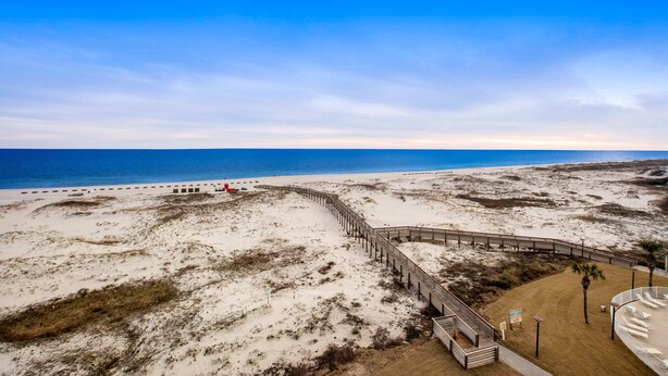 Ein Strand mit einer Holzpromenade, die zu einem Sandbereich führt, einem klaren Himmel und dem Meer im Hintergrund.